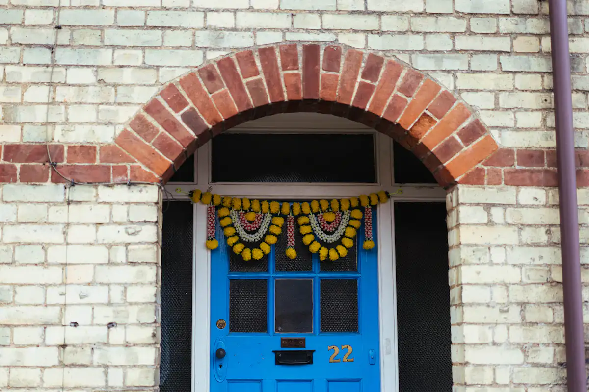 A bright blue door with a yellow marigold garland under a brick archway — The entrance is the only first impression you get