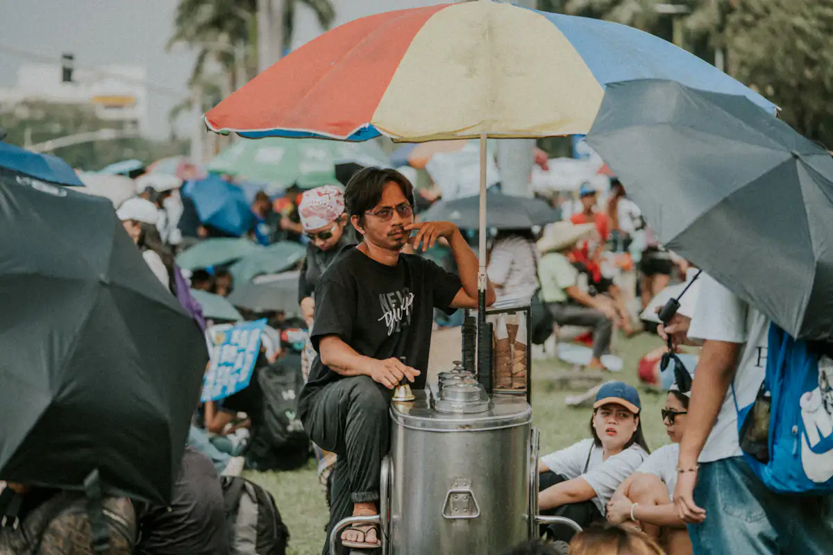 Man with cart under colorful umbrella amidst crowd — Kulfi and gola carts