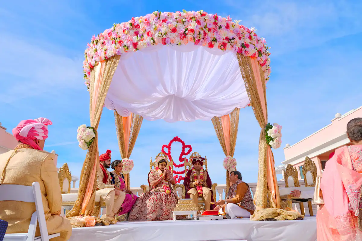 A couple in traditional wedding attire sitting under a floral canopy during a ceremony — A mandap built for the camera as well as the ritual