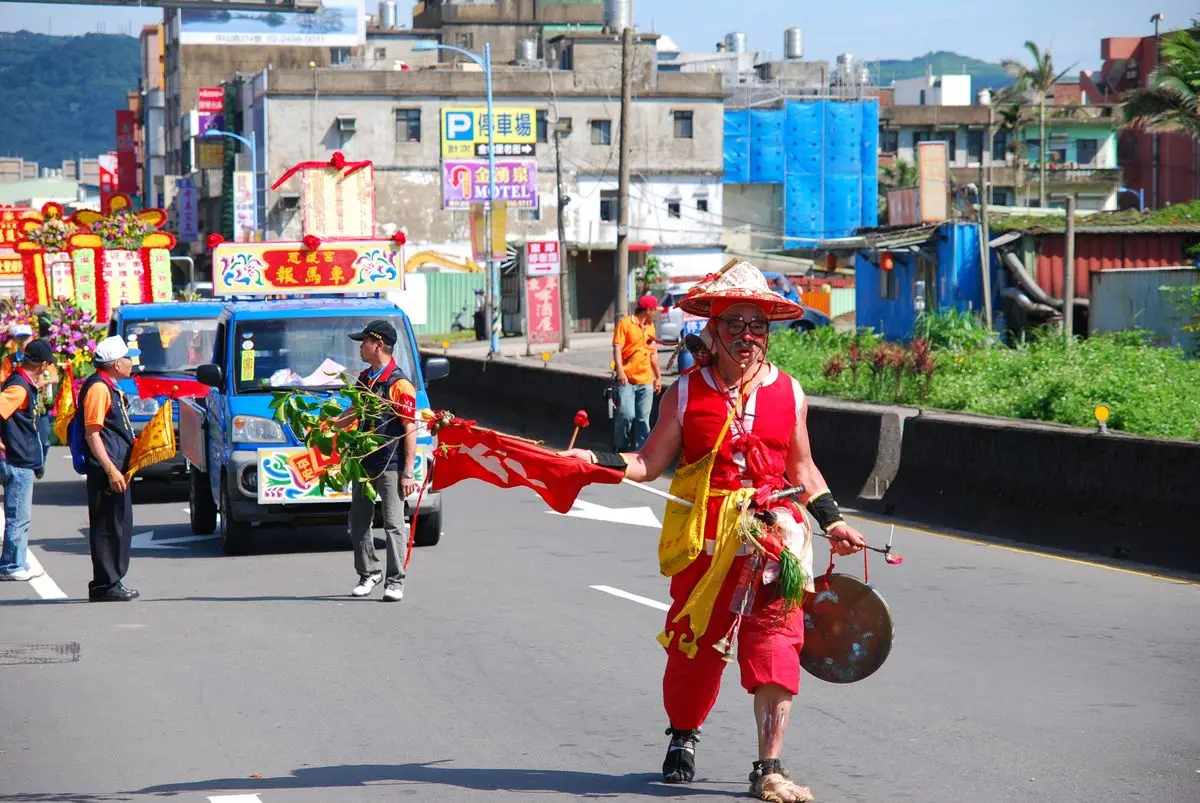 A lively cultural parade with colorful costumes and decorated vehicles in a city street. — The mascot in the baraat