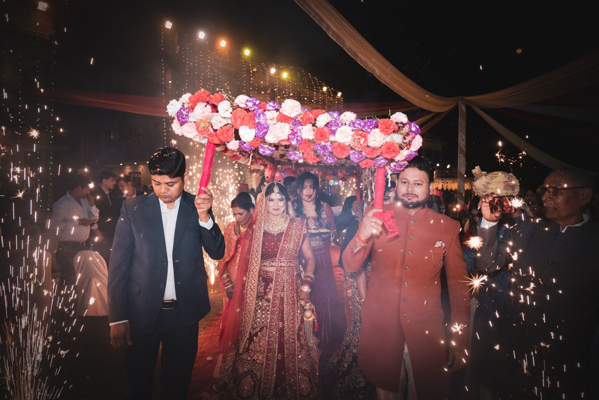 A colorful Indian wedding procession with bride and attendees under flower canopy, surrounded by sparklers. — Phoolon ki chaadar, done so it does not sag