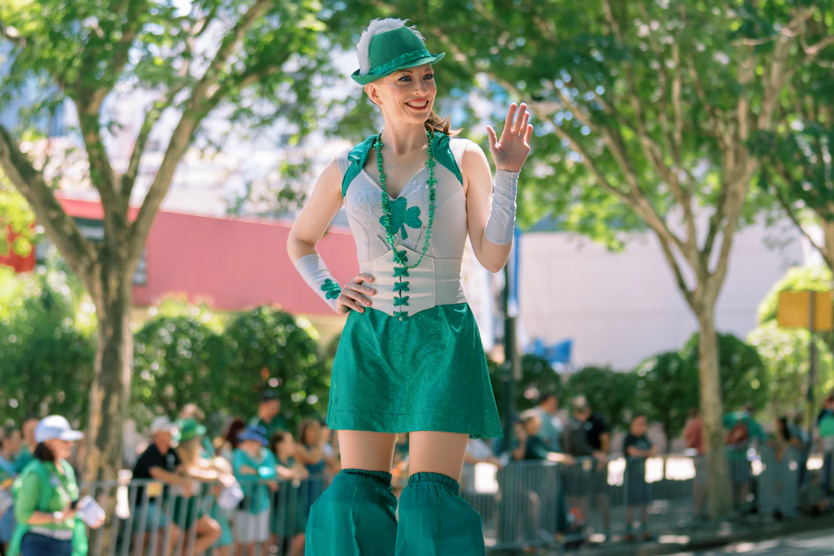 Woman in green costume on stilts waving at parade — Stilt walkers, and the camel version