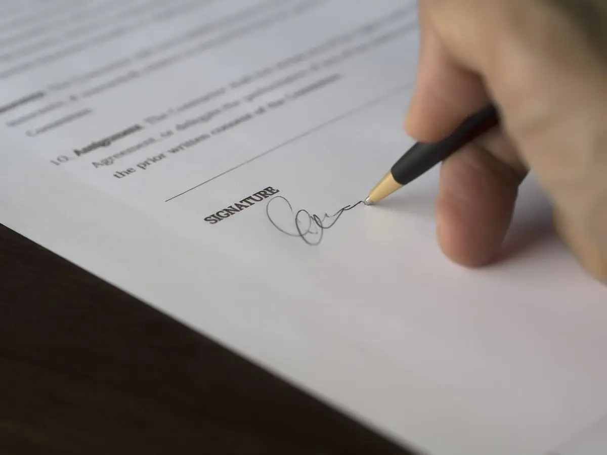 A hand signs a formal contract with a pen on a wooden desk. — A payment schedule that keeps leverage
